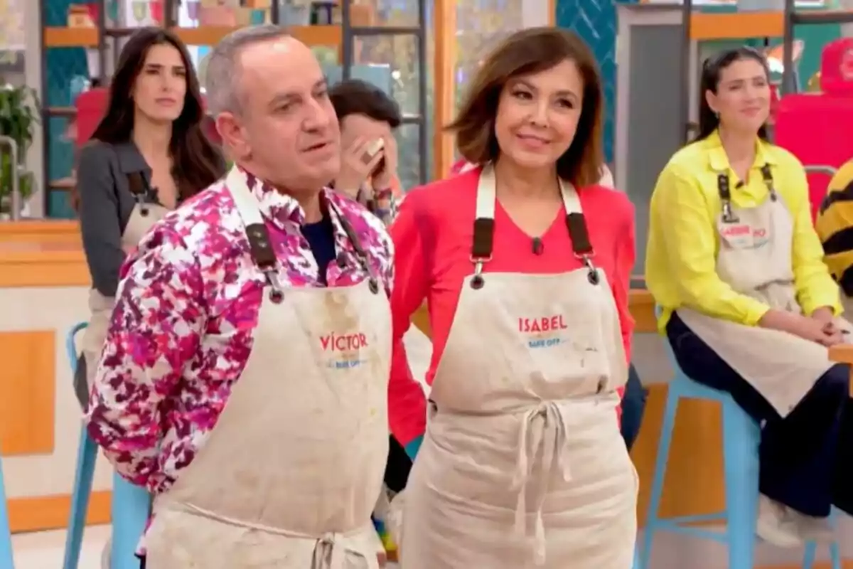 Víctor Sandoval e Isabel Gemio con delantales en un set de cocina, uno de ellas lleva una camisa colorida y la otra un suéter rojo en 'Bake Off: Famosos al horno'.