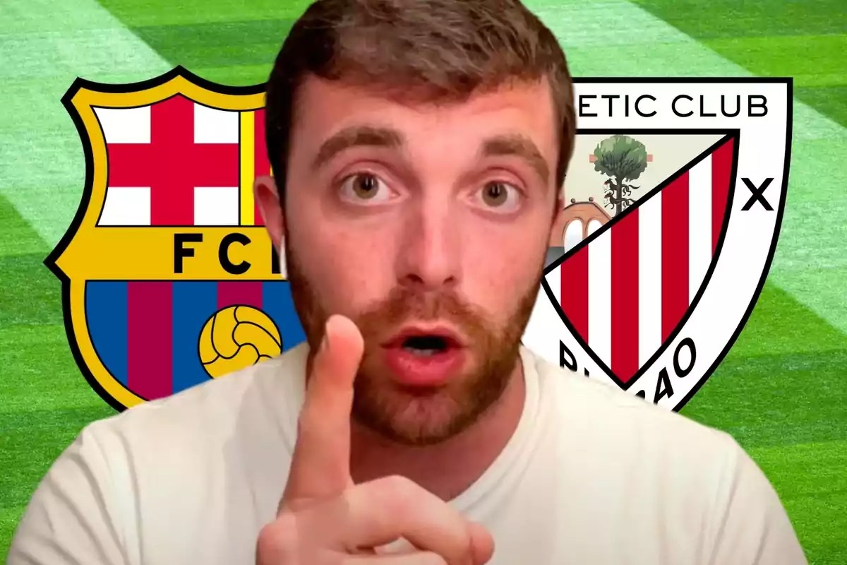 Un home amb barba i samarreta blanca assenyala amb el dit índex cap a la càmera, amb els escuts del FC Barcelona i l?Athletic Club de Bilbao de fons sobre un camp de futbol.