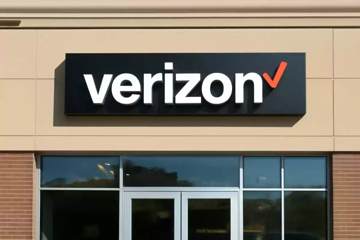 Fachada de una tienda con el logotipo de Verizon en un cartel negro sobre una pared de ladrillo y paneles beige. Fachada de una tienda con el logotipo de Verizon en un cartel negro sobre una pared de ladrillo y paneles beige.