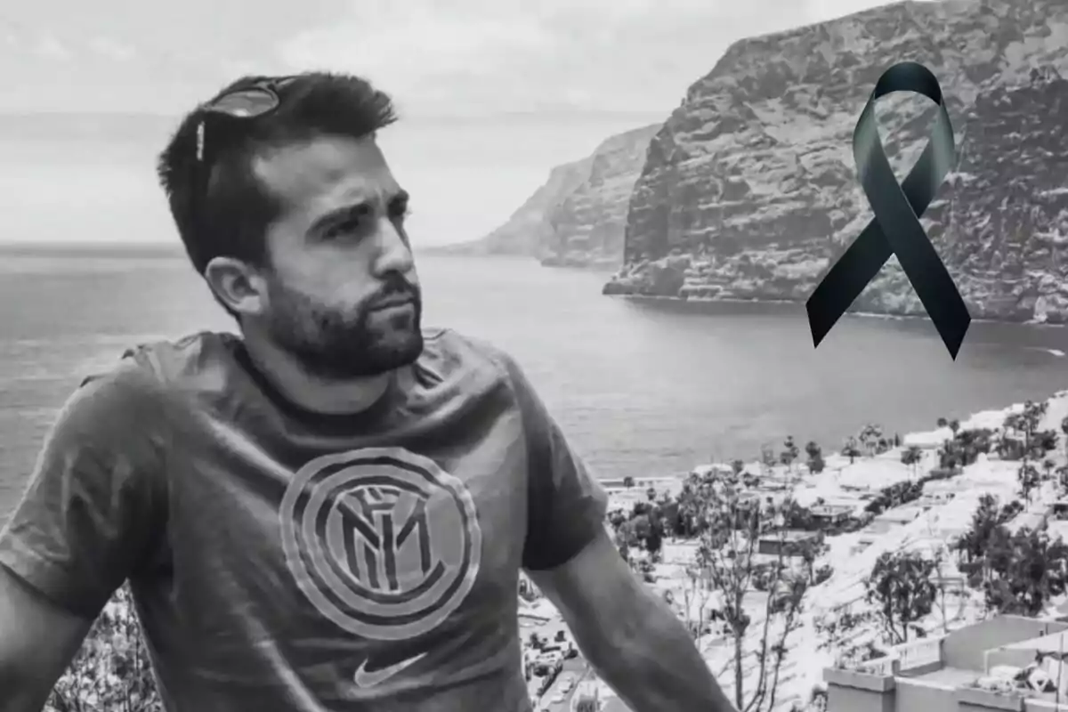 Un home amb samarreta d'un equip de futbol i ulleres de sol al cap mira cap a l'horitzó en un paisatge costaner amb penya-segats i un llaç negre superposat a la imatge.