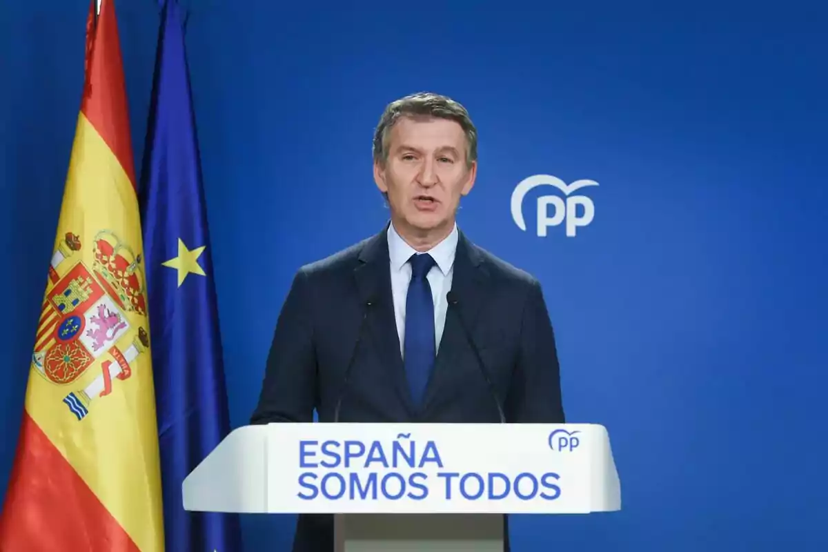 Un home en un podi amb les banderes d?Espanya i la Unió Europea de fons i el logotip del PP.