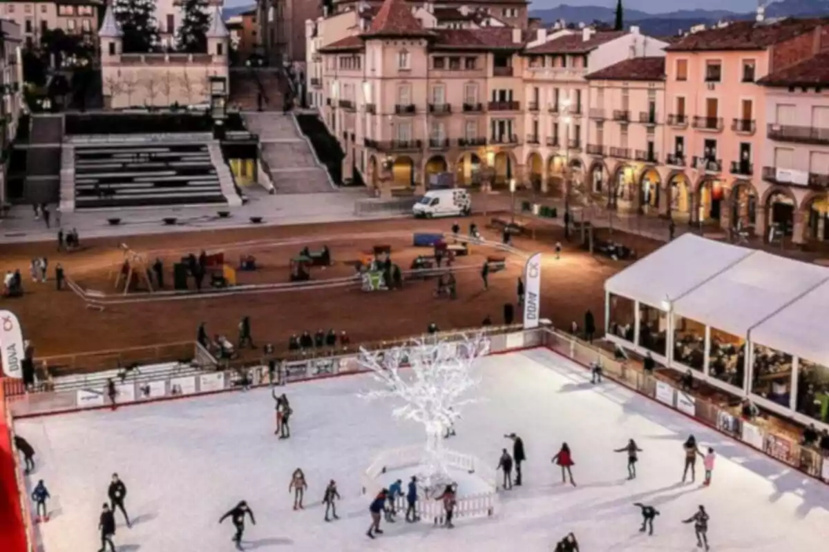 Persones patinant sobre gel en una pista exterior envoltada d'edificis històrics i una plaça il·luminada.