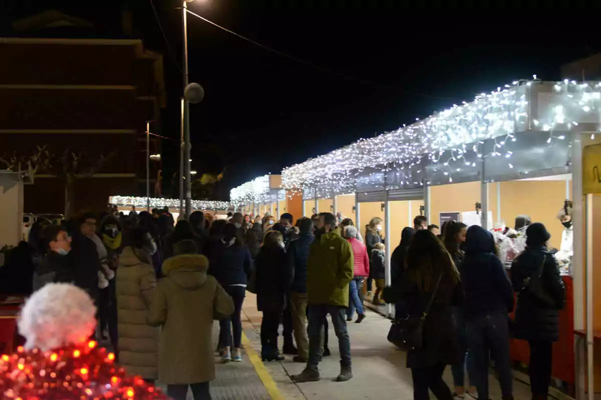 Una multitud de persones passeja per un mercat nocturn a l'aire lliure amb llums decoratives blanques a les parades.