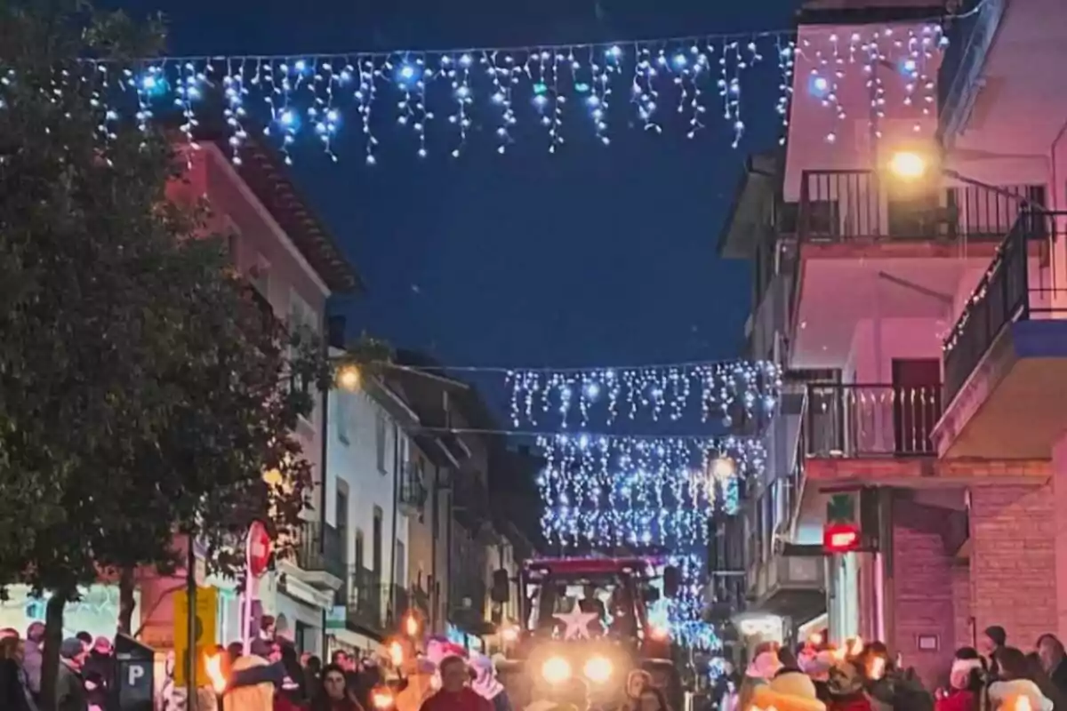 Un carrer decorat amb llums nadalenques penjants i un grup de persones caminant amb torxes.