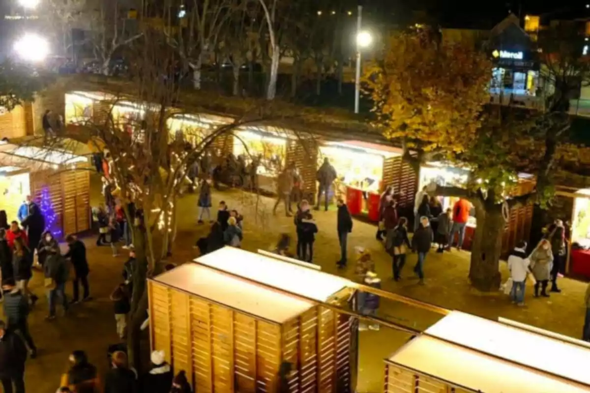 Una feria nocturna al aire libre con puestos de madera iluminados y personas paseando entre ellos.