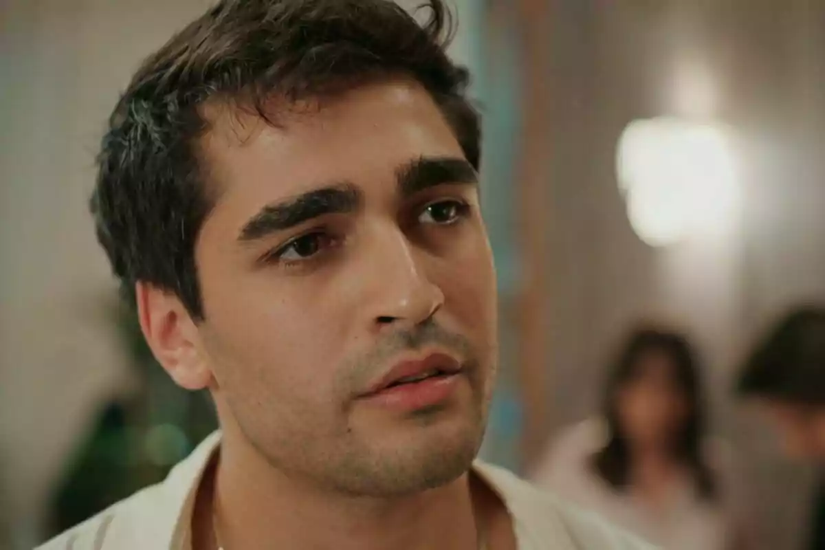 Ferit de cabells foscos i expressió seriosa en un ambient interior desenfocat a Una nova vida Ferit de cabells foscos i expressió seriosa en un ambient interior desenfocat a Una nova vida