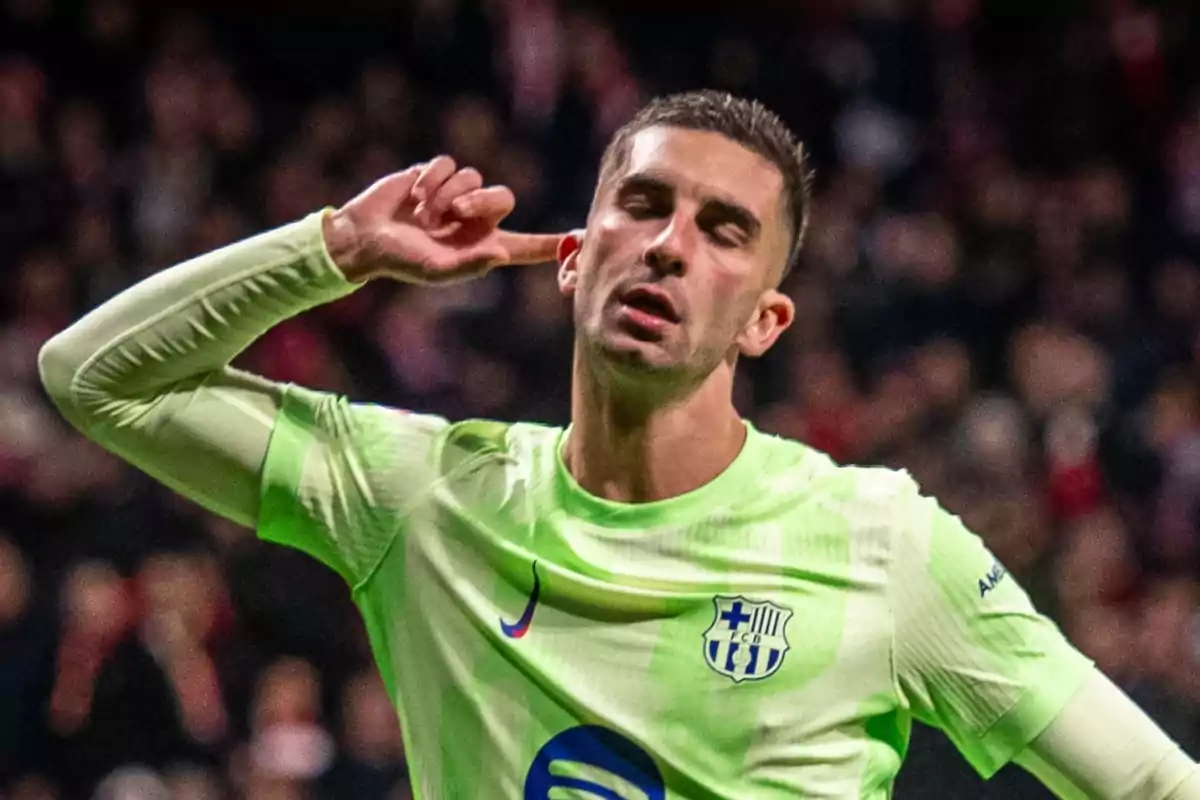 Un jugador de fútbol con uniforme verde claro celebra llevándose la mano a la oreja en un estadio lleno de espectadores.