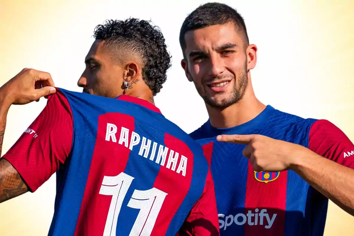 Two players wearing FC Barcelona jerseys, one displaying the name "Raphinha" on his back and the other pointing at him.