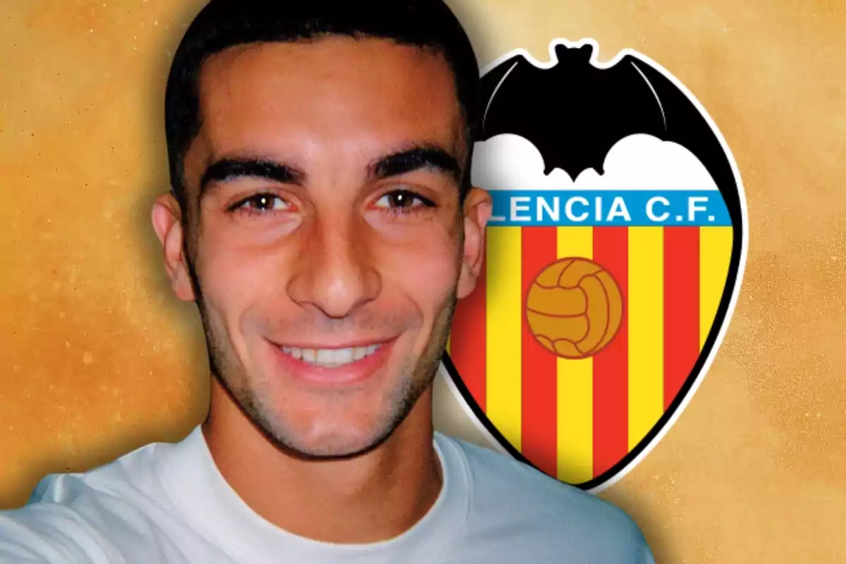 Jove somrient amb samarreta blanca davant de l’escut del València Club de Futbol sobre fons taronja