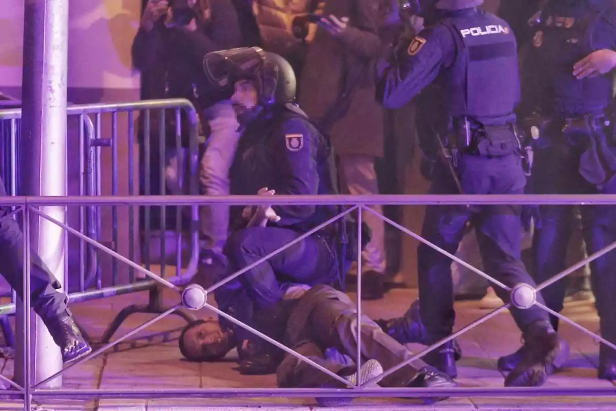 Un policia antiavalots amb la cara pixelada reté un manifestant davant de la seu del PSOE al carrer Ferraz de Madrid