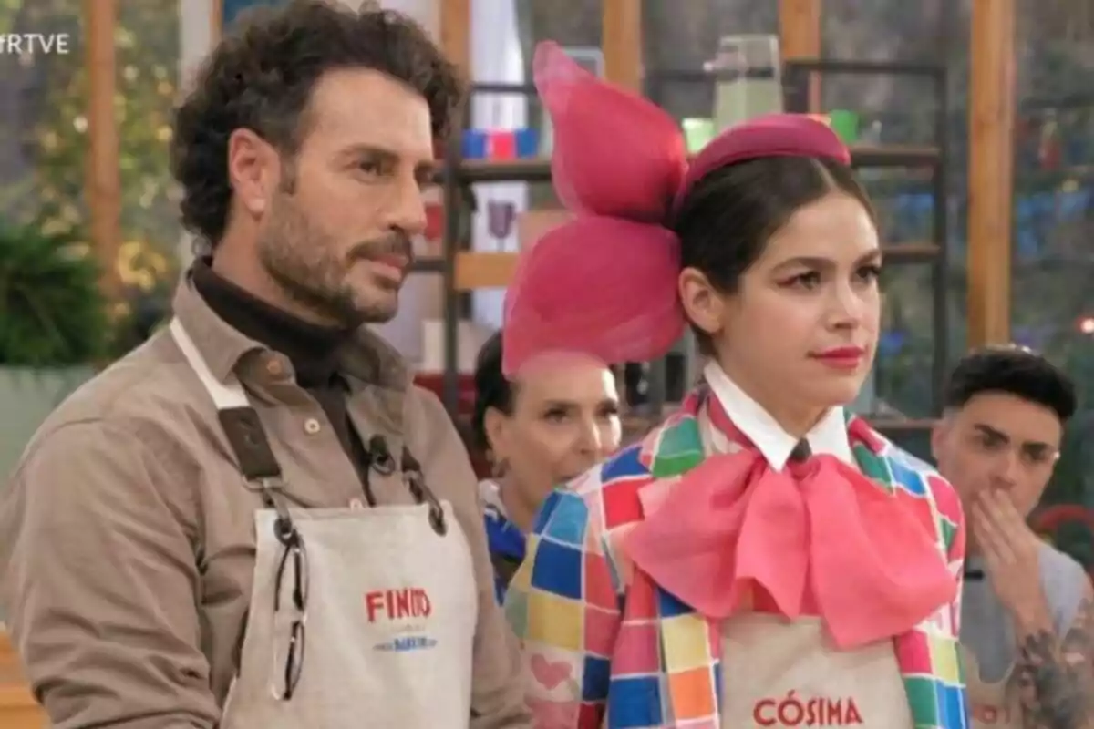 Finito de Córdoba y Cósima Ramírez con delantales en Bake Off: famosos al horno, una de ellas lleva un atuendo colorido con un gran lazo rosa en la cabeza.