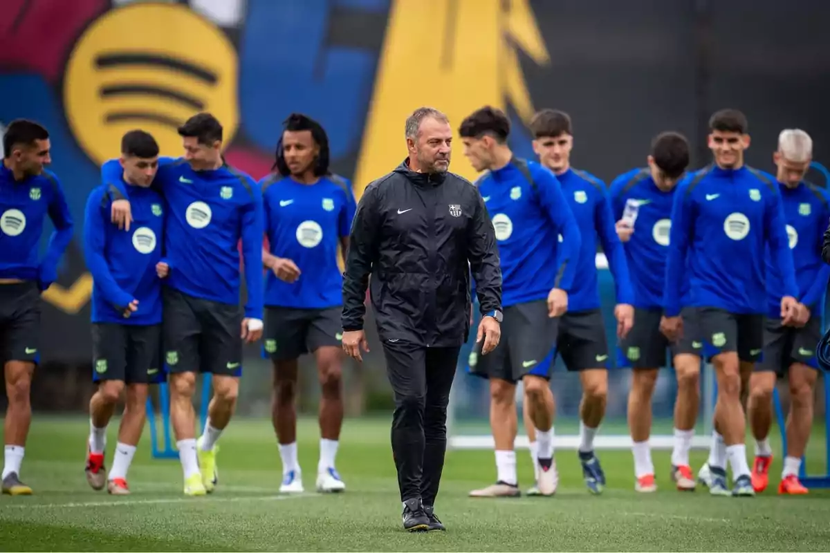 Entrenador de futbol caminant al davant mentre jugadors del Barcelona s’entrenen al camp amb uniforme blau Entrenador de futbol caminant al davant mentre jugadors del Barcelona s’entrenen al camp amb uniforme blau