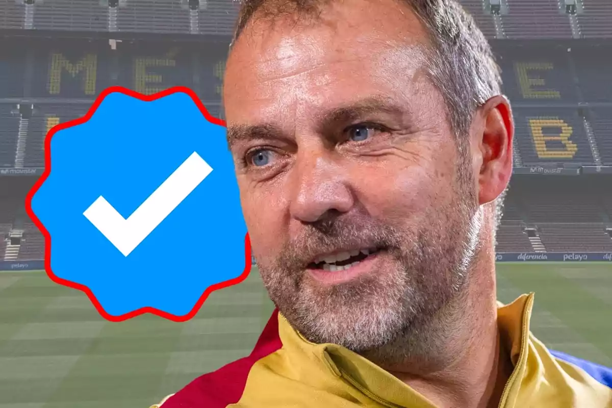 Un hombre sonriente con barba y cabello corto en un estadio de fútbol con un símbolo de verificación azul al lado.