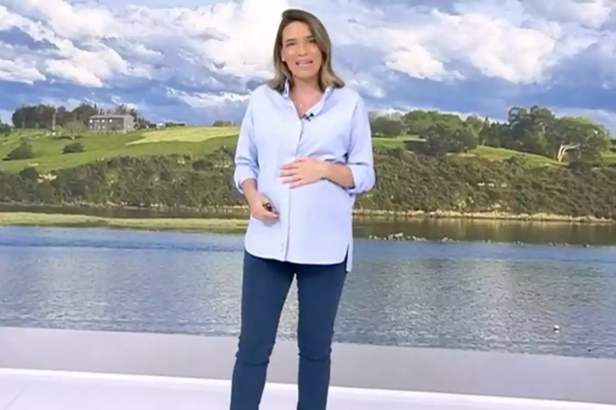 Flora González embarassada està dempeus davant d'un fons que mostra un paisatge amb un riu i turons verds sota un cel ennuvolat a 'Informatius Telecinco'. Flora González embarassada està dempeus davant d'un fons que mostra un paisatge amb un riu i turons verds sota un cel ennuvolat a 'Informatius Telecinco'.