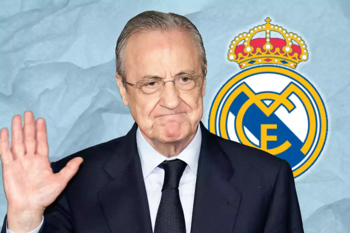 Un home amb vestit fosc i corbata aixeca la mà davant un fons amb l?escut del Reial Madrid.
