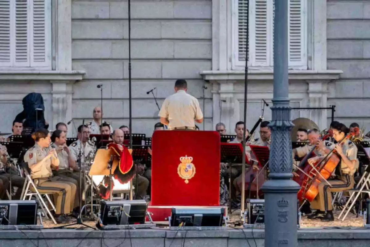 Una banda militar uniformada interpreta música a l’aire lliure sota la direcció d’un director davant d’un edifici històric. Una banda militar uniformada interpreta música a l’aire lliure sota la direcció d’un director davant d’un edifici històric.
