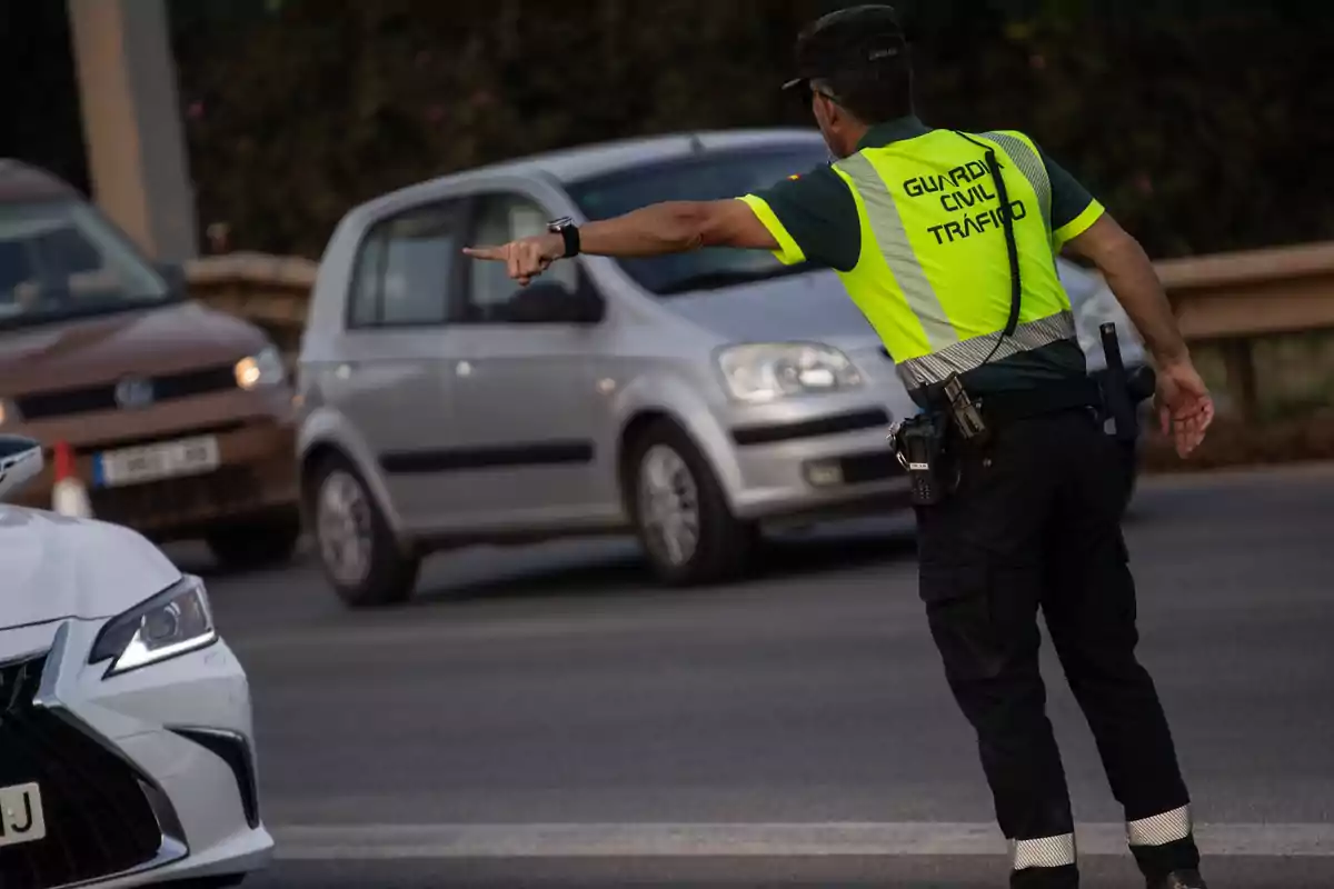 Agent de la Guàrdia Civil de Trànsit dirigint el trànsit en una carretera mentre diversos cotxes circulen al voltant Agent de la Guàrdia Civil de Trànsit dirigint el trànsit en una carretera mentre diversos cotxes circulen al voltant