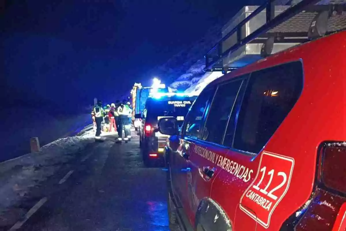 Vehículos de emergencia y personal de rescate trabajando en una carretera nevada durante la noche.