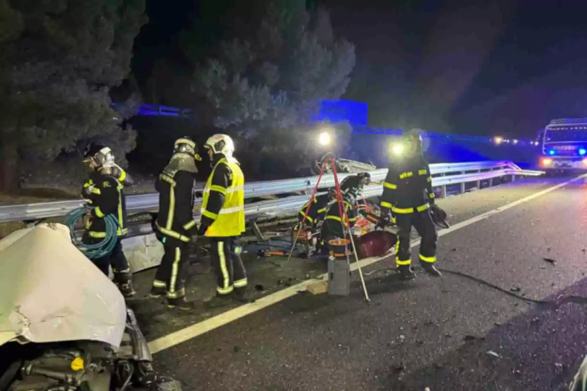 Bombers treballant a l'escena d'un accident de trànsit en una carretera a la nit.