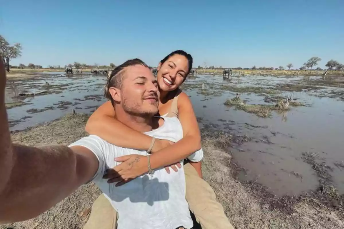 Una parella somrient es pren una selfie en un entorn natural amb aigua i vegetació.