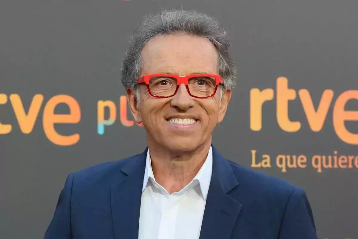 Fotografia de Jordi Hurtado en primer pla, mirant a càmera, somrient i usant un vestit amb unes ulleres de color vermell