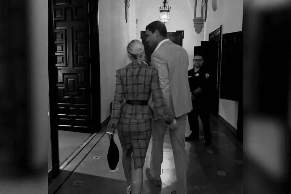 Jessica Goicoechea and Manu Moreno walking hand in hand down an elegant hallway with a guard in the background. Jessica Goicoechea and Manu Moreno walking hand in hand down an elegant hallway with a guard in the background.