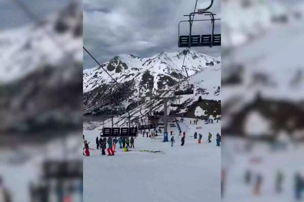 Persones esquiant en una estació d'esquí amb muntanyes nevades i telecadires al fons a Osca.