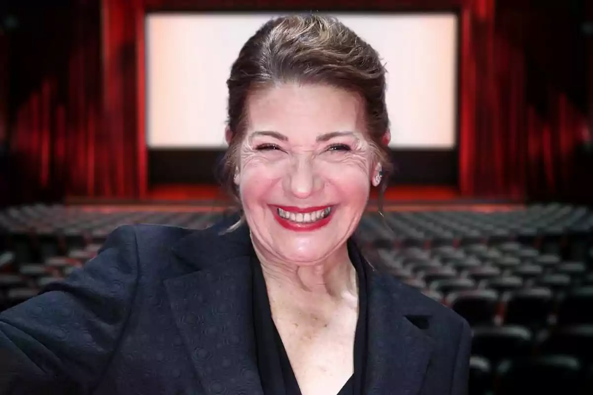 A smiling woman in an empty movie theater with a large screen in the background.