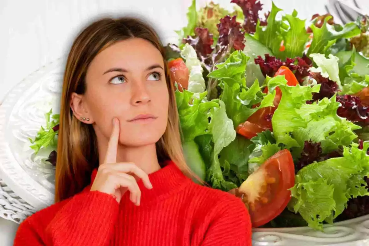 Dona pensativa amb un suèter vermell davant d'un plat d'amanida.