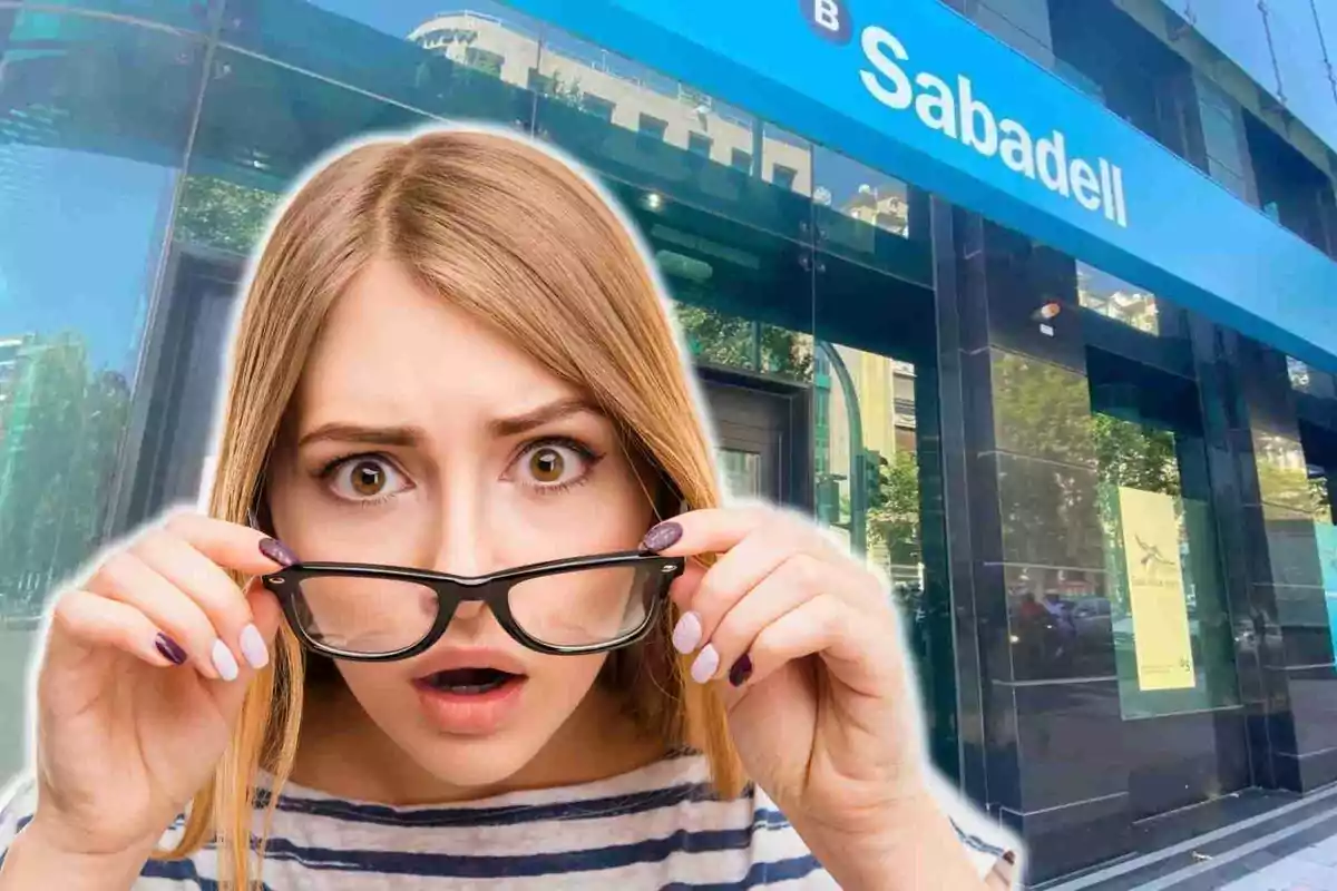 Una mujer con expresión de sorpresa sostiene sus gafas frente a un edificio con el letrero de Sabadell.