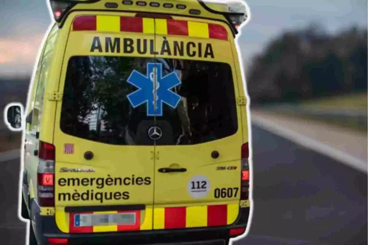 Una ambulància groga amb la paraula "AMBULÀNCIA" a la part superior del darrere i "emergències mèdiques" a la part inferior, amb una estrella blava de la vida al centre i el número d'emergència 112.