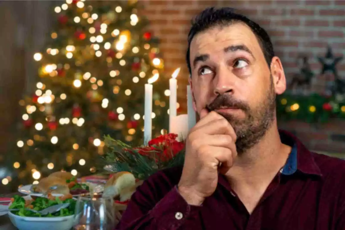 Hombre pensativo frente a una mesa navideña con velas y un árbol de Navidad iluminado al fondo.