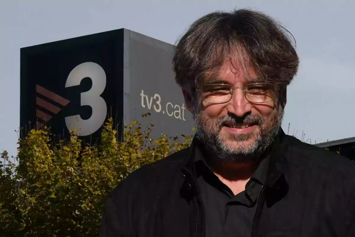 Un hombre con barba y gafas sonríe frente a un edificio con el logo de TV3.