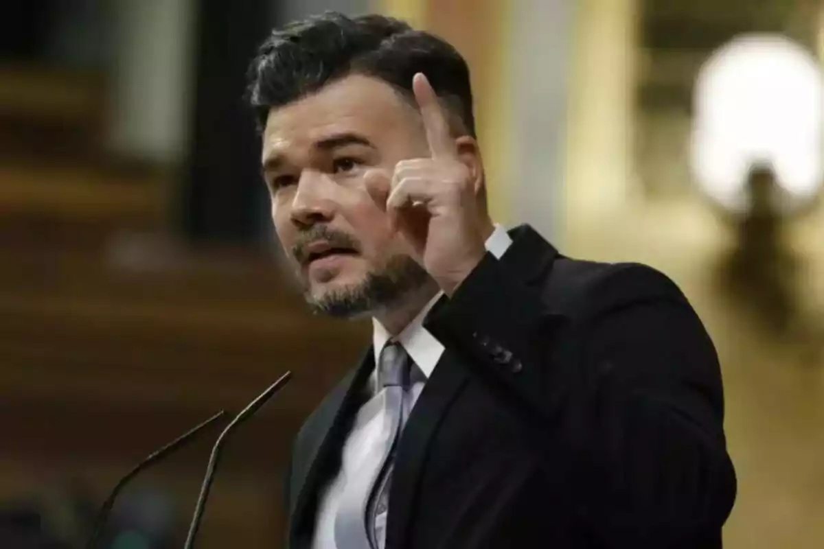 Un home amb vestit fosc i corbata parla en un faristol aixecant un dit.