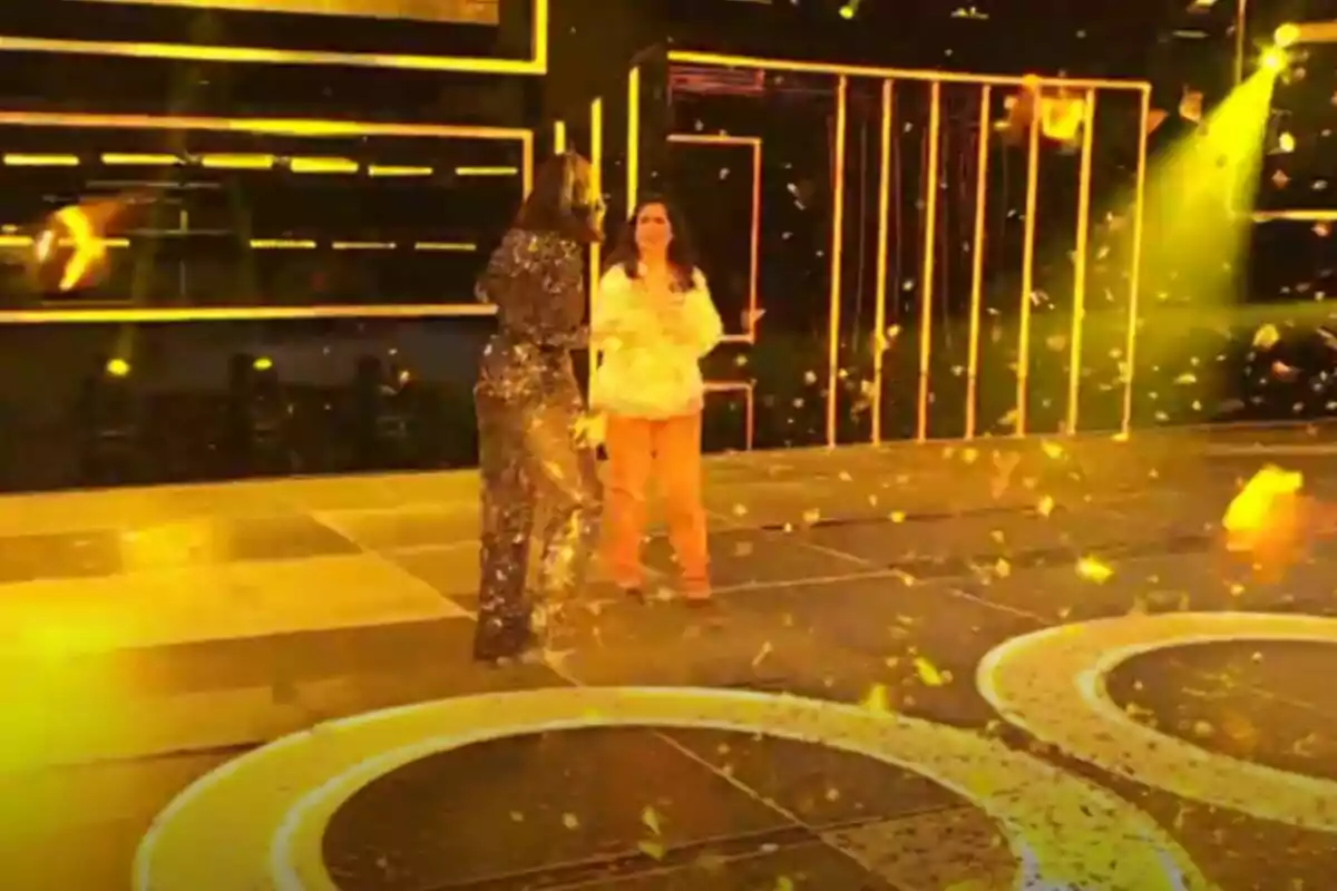 Mercedes i Chenoa en un escenari il·luminat amb llums grogues i confeti daurat caient al voltant a The Floor. Mercedes i Chenoa en un escenari il·luminat amb llums grogues i confeti daurat caient al voltant a The Floor.