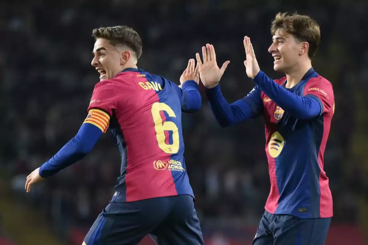 Two soccer players celebrate on the field in blue and red uniforms.