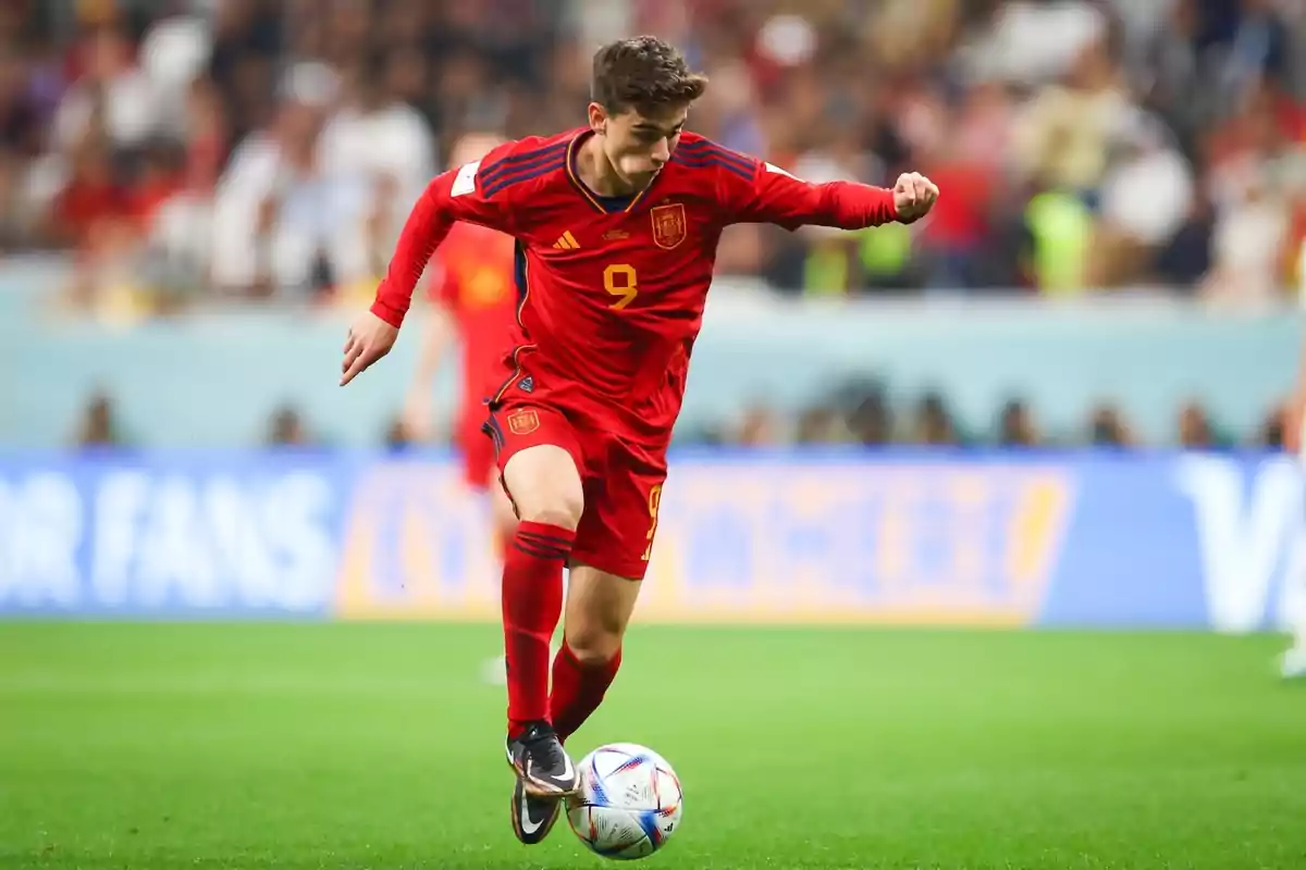 Futbolista de la selecció d’Espanya amb uniforme vermell controlant la pilota durant un partit en un estadi ple d’espectadors Futbolista de la selecció d’Espanya amb uniforme vermell controlant la pilota durant un partit en un estadi ple d’espectadors
