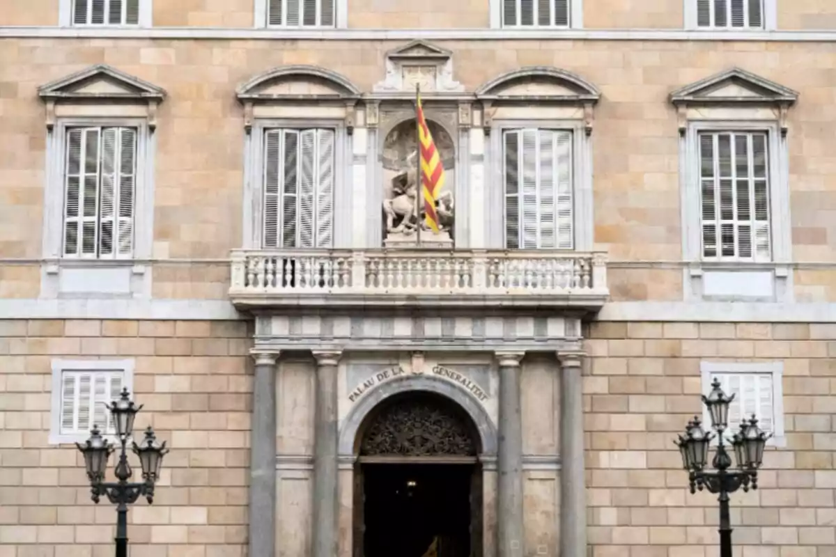 Fachada de un edificio histórico con una bandera en el balcón y una entrada con columnas y farolas. Fachada de un edificio histórico con una bandera en el balcón y una entrada con columnas y farolas.