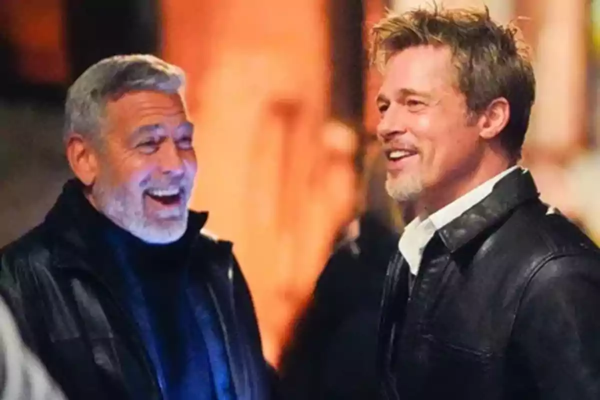 George Clooney i Brad Pitt somriuen i conversen mentre porten jaquetes de cuir en un ambient il·luminat. George Clooney i Brad Pitt somriuen i conversen mentre porten jaquetes de cuir en un ambient il·luminat.