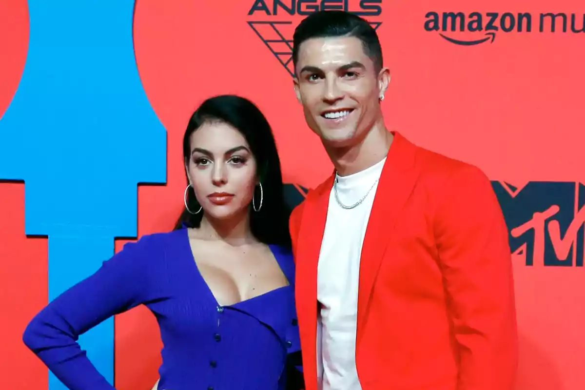 Georgina Rodríguez and Cristiano Ronaldo posing together at an event with a red and blue background.