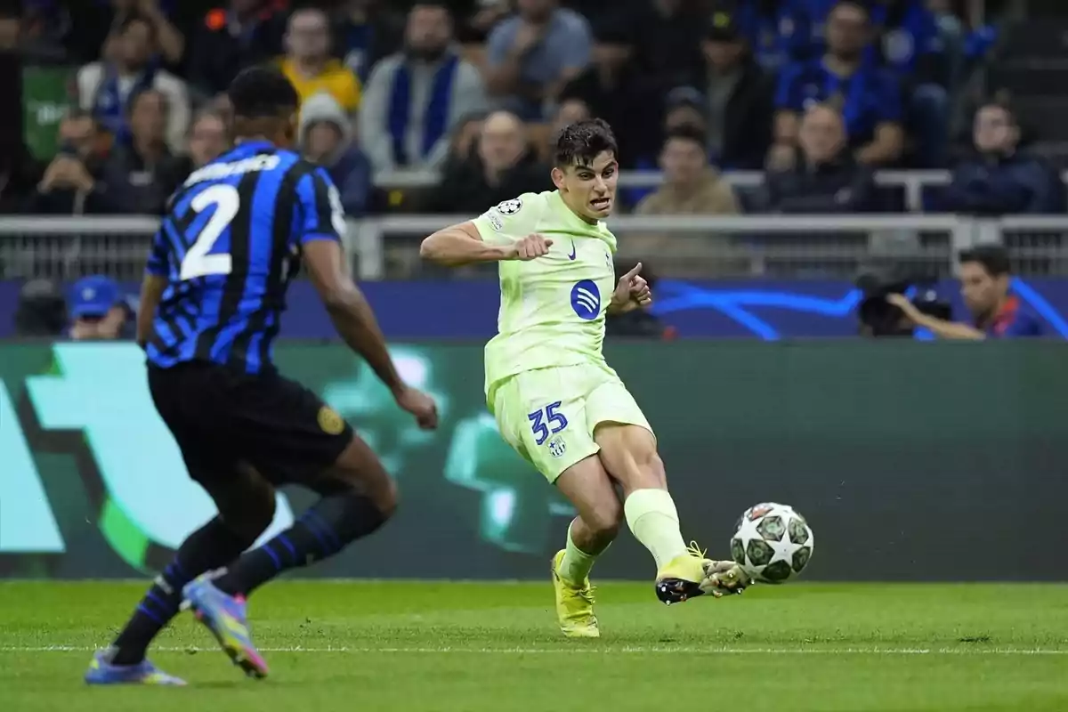 A player in a light uniform controls the ball while an opponent in a black and blue striped uniform approaches in a stadium full of spectators. A player in a light uniform controls the ball while an opponent in a black and blue striped uniform approaches in a stadium full of spectators.