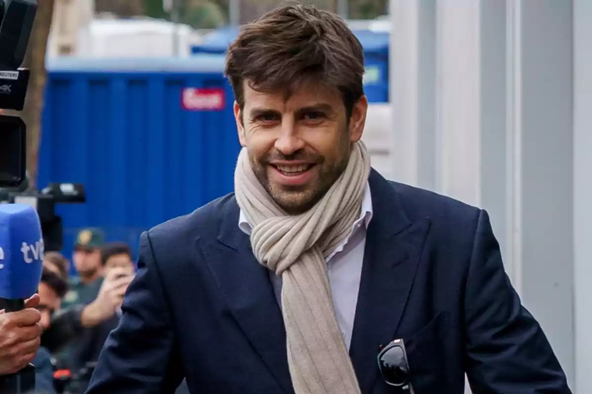 Gerard Piqué sonriente con barba y bufanda clara lleva un traje oscuro mientras camina al aire libre. Gerard Piqué sonriente con barba y bufanda clara lleva un traje oscuro mientras camina al aire libre.