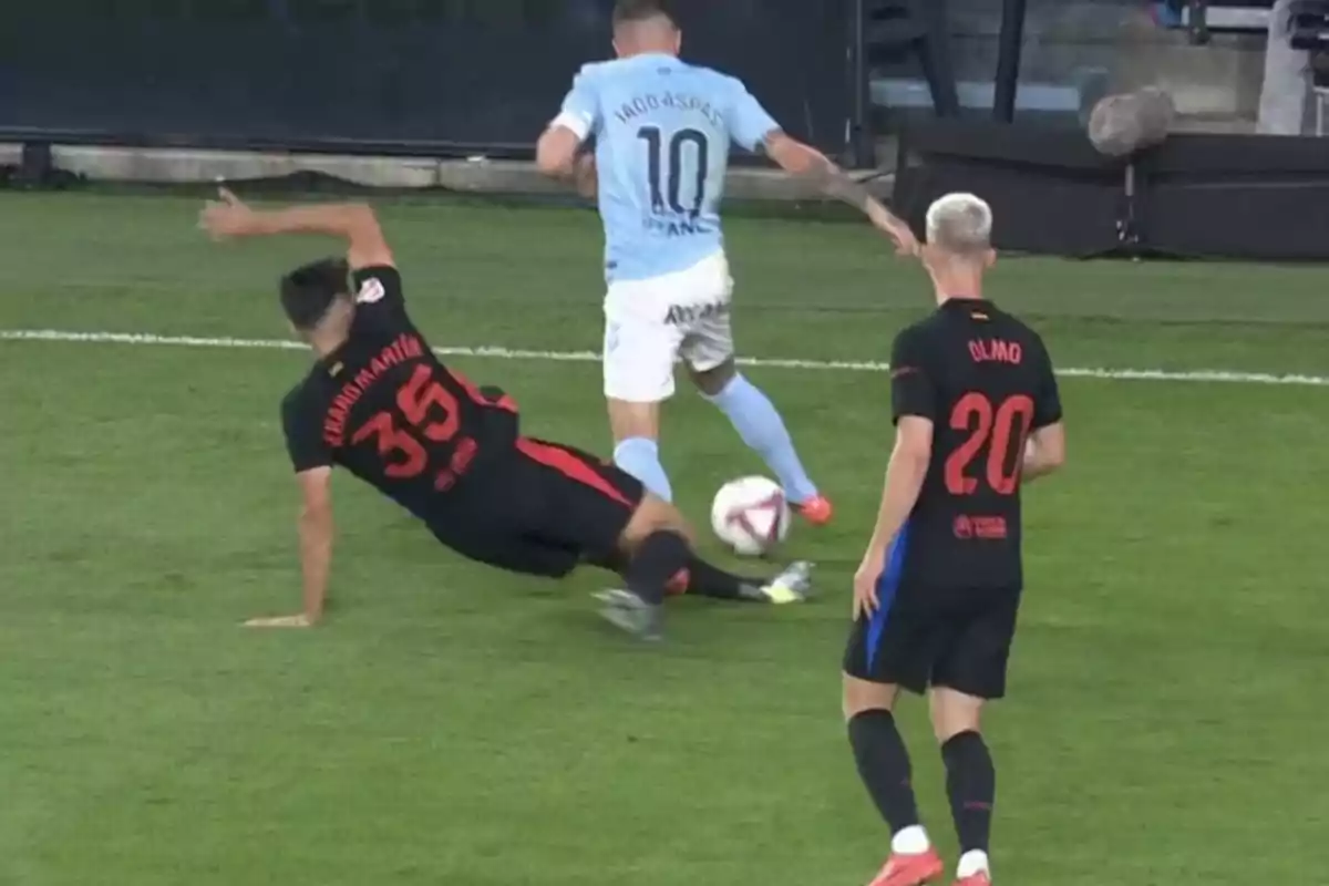 Un jugador de futbol amb samarreta celeste porta la pilota mentre és desafiat per un oponent que cau a terra, un altre jugador observa la jugada. Un jugador de futbol amb samarreta celeste porta la pilota mentre és desafiat per un oponent que cau a terra, un altre jugador observa la jugada.