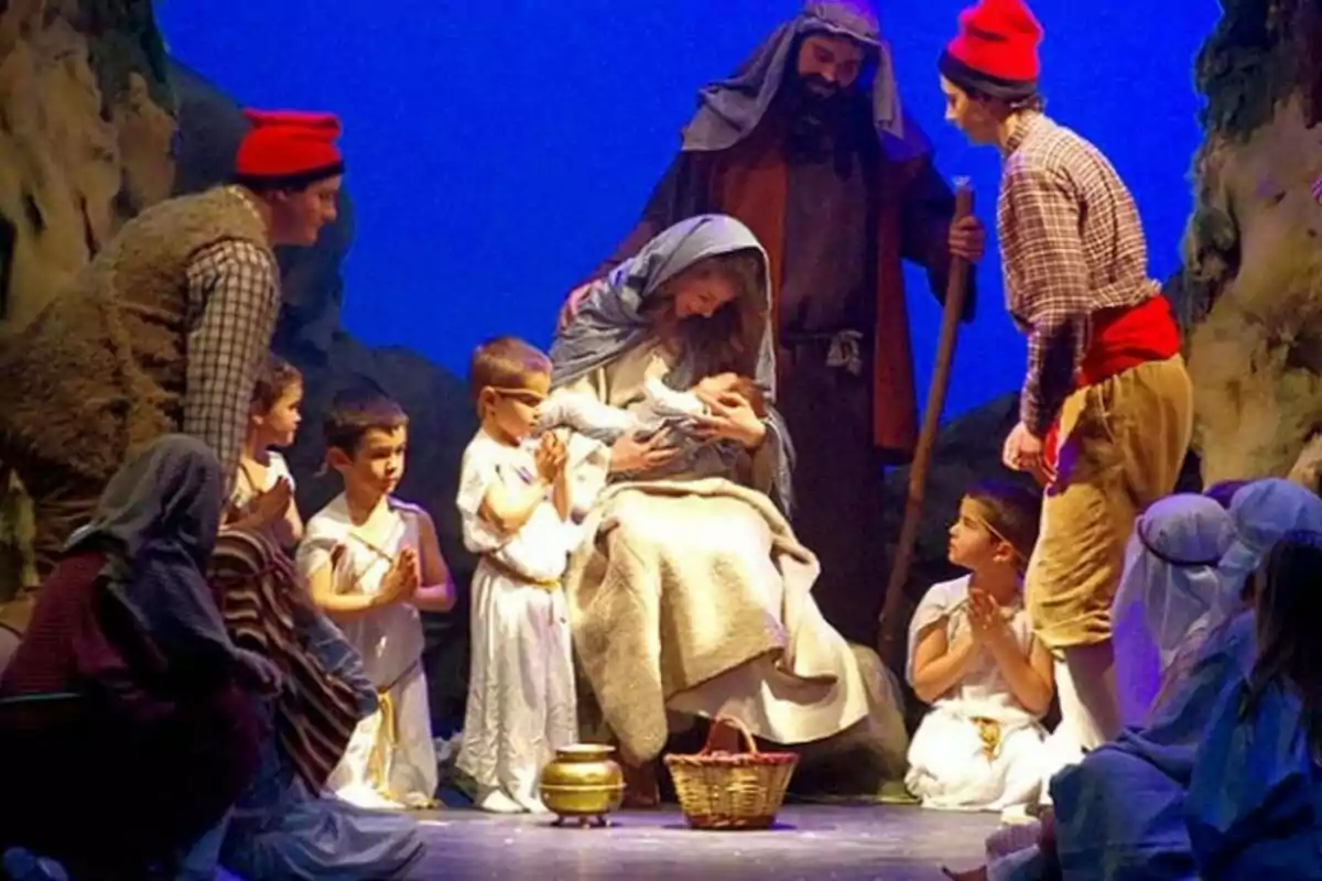 Una representació teatral d'un naixement amb personatges vestits amb vestits tradicionals envoltant un nadó en un pessebre.