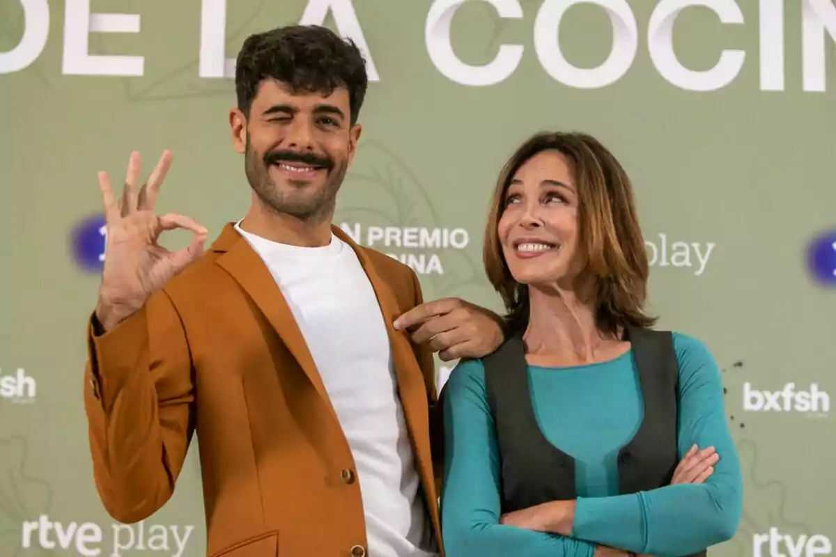 Germán González i Lydia Bosch posen davant d'una paret verda amb text, una fa un gest d'"OK" amb la mà i pica l'ullet mentre l'altra somriu en la presentació d'El Gran Premi de la Cuina.