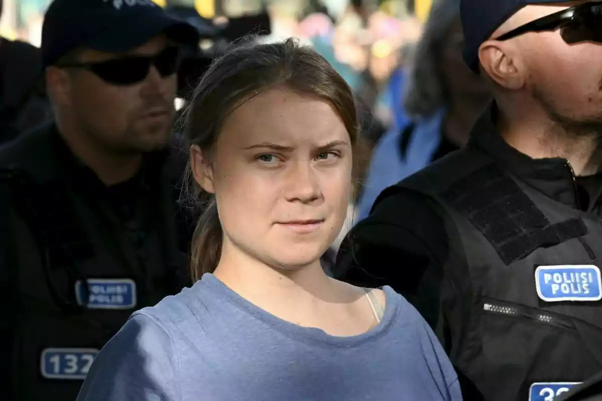 Greta Thunberg amb una samarreta blau clar envoltada de policies amb ulleres de sol i armilles negres en un esdeveniment a l’aire lliure. Greta Thunberg amb una samarreta blau clar envoltada de policies amb ulleres de sol i armilles negres en un esdeveniment a l’aire lliure.