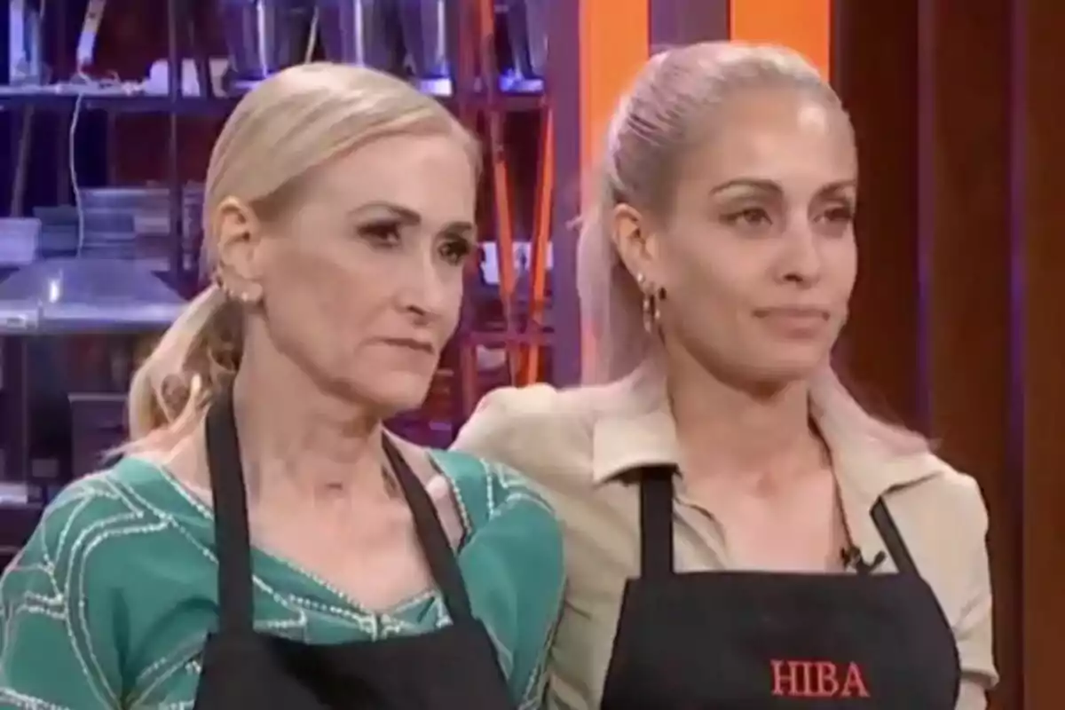 Cristina Cifuentes i Hiba Abouk amb davantals negres estan drets en un entorn de cuina a MasterChef Celebrity.