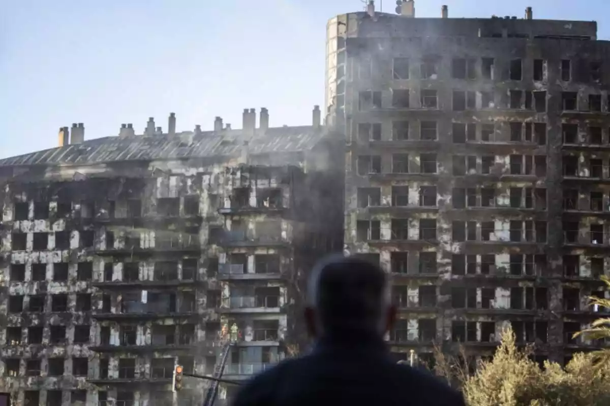Un home en primer pla observant l'edifici d'habitatges cremat a València