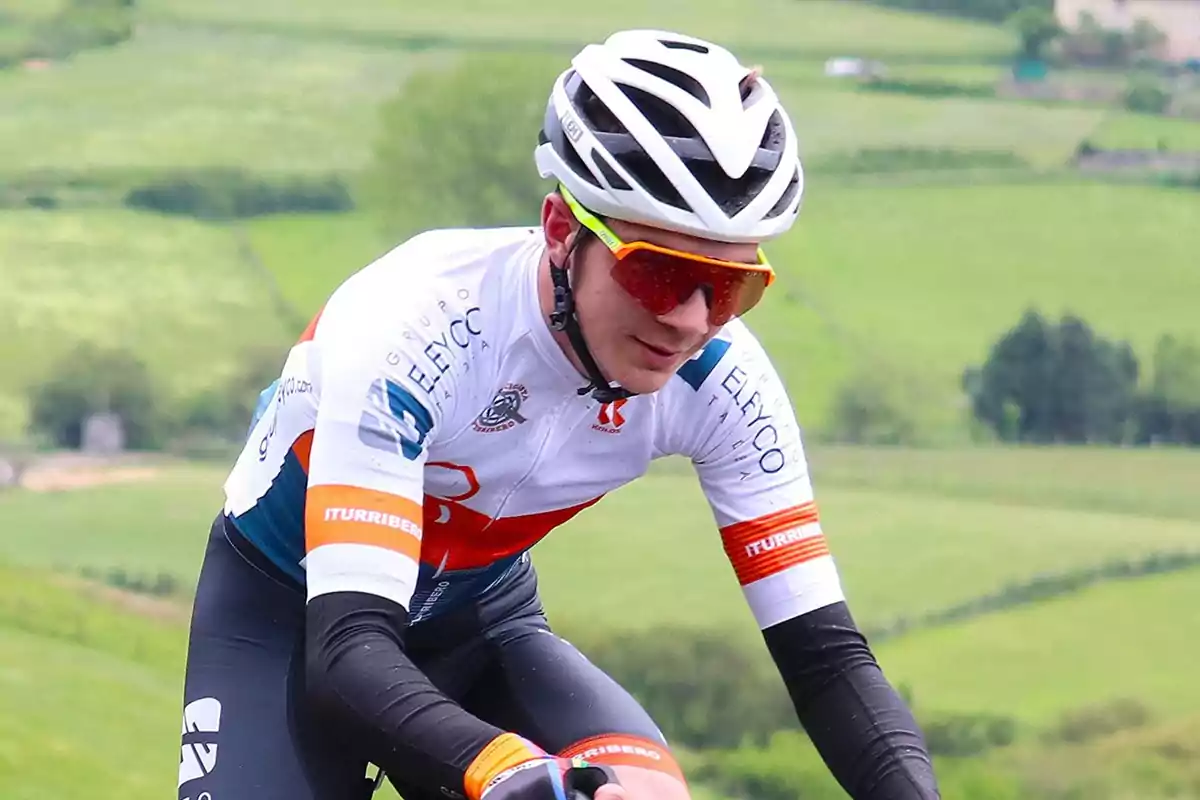 Ciclista amb casc blanc i ulleres esportives muntant en bicicleta en un entorn rural verd Ciclista amb casc blanc i ulleres esportives muntant en bicicleta en un entorn rural verd