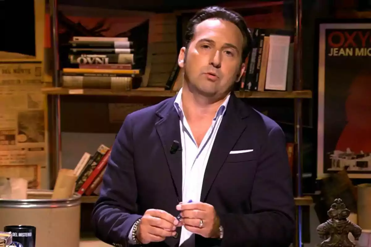 Iker Jiménez de cabell fosc amb americana blau marí i camisa blanca dret en un estudi amb prestatgeries plenes de llibres i cartells a la paret a Cuarto Milenio Iker Jiménez de cabell fosc amb americana blau marí i camisa blanca dret en un estudi amb prestatgeries plenes de llibres i cartells a la paret a Cuarto Milenio
